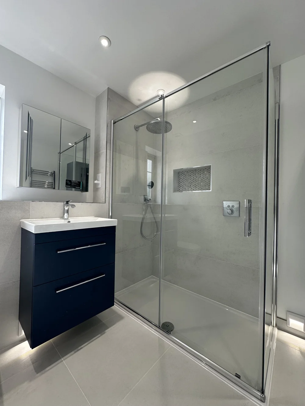 Modern ensuite with navy floating vanity, mirrored cabinet and sliding-door shower enclosure — bathroom installation Haslemere