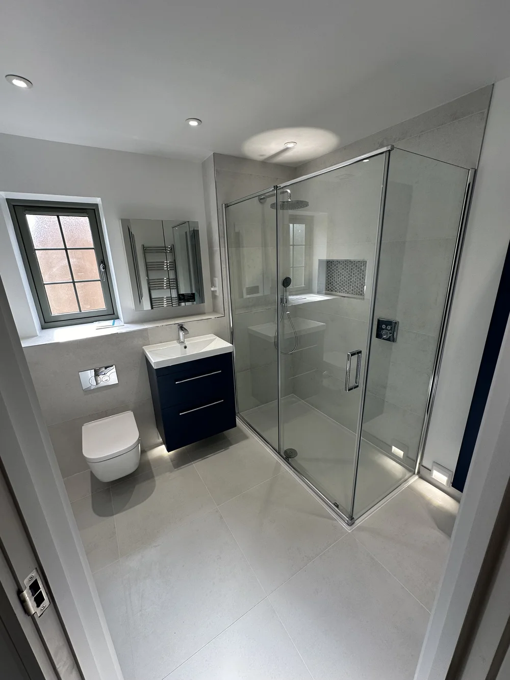 Fitted ensuite with navy vanity, wall-hung WC and corner shower enclosure — bathroom installation Haslemere